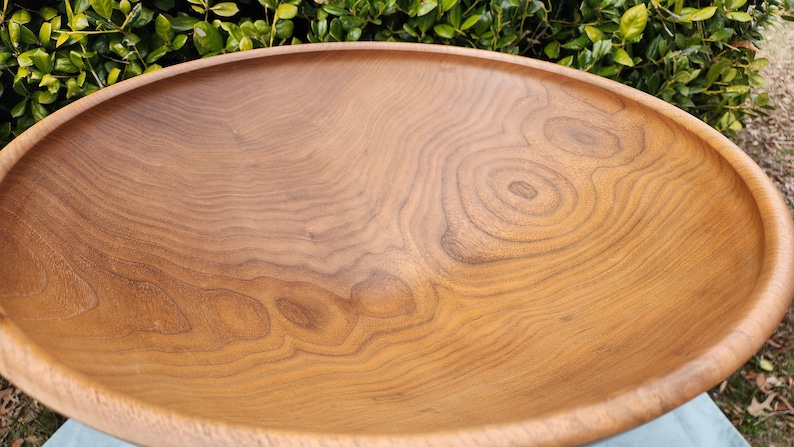 May include: A large, wooden bowl with a natural, light brown finish. The bowl is made of wood with a beautiful grain pattern.