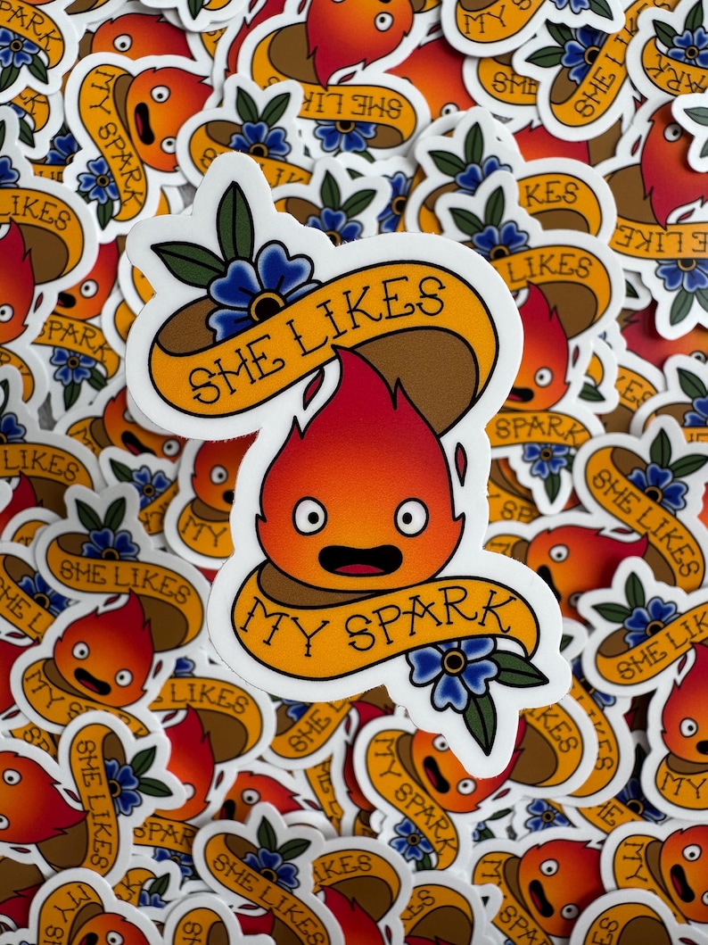 May include: A collection of stickers featuring a cartoon flame character with the text "SHE LIKES MY SPARK" on a banner. The stickers are in shades of orange, red, brown, and yellow, with blue floral accents. The stickers are a fun, whimsical design.