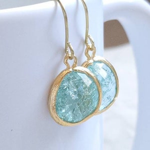 Peut inclure: Boucles d'oreilles dorées avec des pierres en forme de larme bleu clair. Les pierres ont une texture scintillante et facetée.