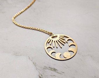 May include: A gold necklace with a circular pendant featuring a sun and moon design. The pendant is cut out to show the sun's rays and the phases of the moon.