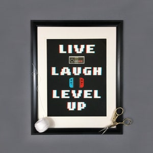 May include: Black framed picture with a white mat and a black background. The text "LIVE LAUGH LEVEL UP" is in a pixelated font with a retro video game controller graphic.