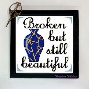 Puede incluir: Un diseño de punto de cruz enmarcado que presenta un jarrón azul y dorado con un efecto craquelado. El texto dice "Roto pero aún hermoso" y está firmado "Sleepless Stitcher".