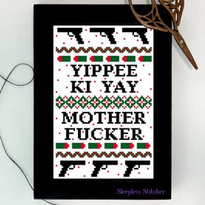 Könnte beinhalten: Ein weißes Kreuzstichmuster mit schwarzem Hintergrund. Das Muster zeigt ein Weihnachtspullover-Design mit dem Text "Yippee Ki Yay Mother Fucker" und einem sich wiederholenden Muster aus Pistolen und Kugeln.