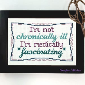 Puede incluir: Un diseño de punto de cruz enmarcado con el texto "I'm not chronically ill I'm medically *fascinating*" en letras color turquesa, morado y negro. El marco es negro y el fondo es blanco. La esquina inferior derecha del marco tiene el texto "Sleepless Stitcher" en letras moradas.