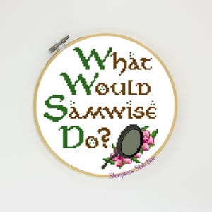Puede incluir: Un aro de bordado blanco con el texto "What Would Samwise Do?" en letras verdes y marrones. Una pequeña ilustración estilizada gris de una sartén con un mango verde y flores rosas está debajo del texto. El texto "Sleepless Stitcher" está en letras moradas en la parte inferior del aro.