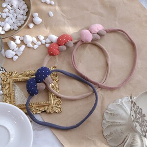May include: Three fabric headbands with mushroom-shaped embellishments. The headbands are in pink, brown, and blue with white polka dots.