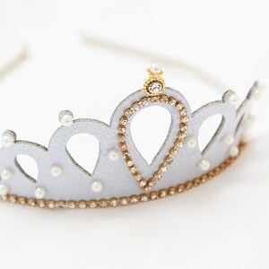 May include: A silver crown headband with a gold center piece and pearl accents. The crown is decorated with rhinestones.