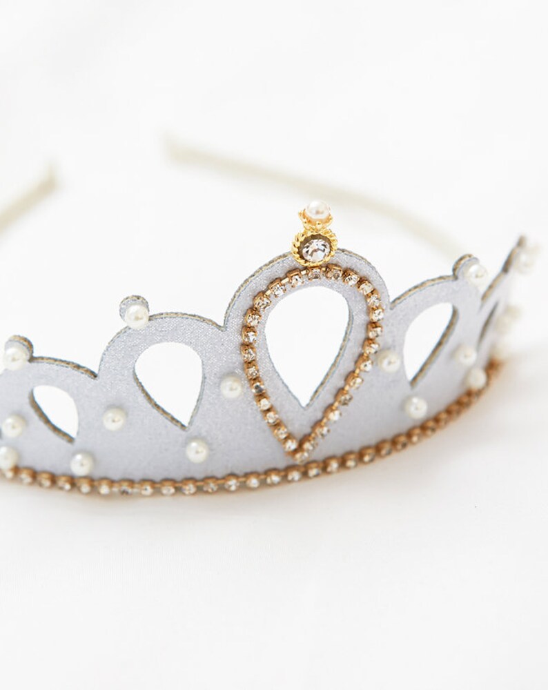 May include: A silver crown headband with a gold center piece and pearl accents. The crown is decorated with rhinestones.