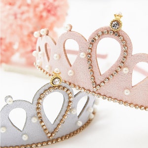 May include: Two princess crowns, one pink and one silver, with rhinestones and pearl accents. Both crowns have a gold crown on top.