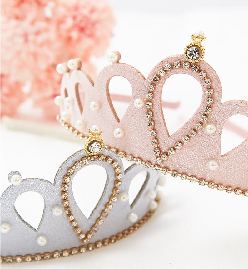 May include: Two princess crowns, one pink and one silver, with rhinestones and pearl accents. Both crowns have a gold crown on top.