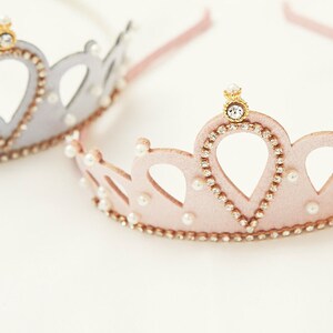 May include: Two princess crowns, one silver and one pink, with pearl and rhinestone accents. The crowns are made of felt and have a headband.