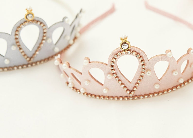 May include: Two princess crowns, one silver and one pink, with pearl and rhinestone accents. The crowns are made of felt and have a headband.