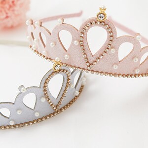 May include: Two princess crowns, one pink and one silver, with gold trim and pearl accents.