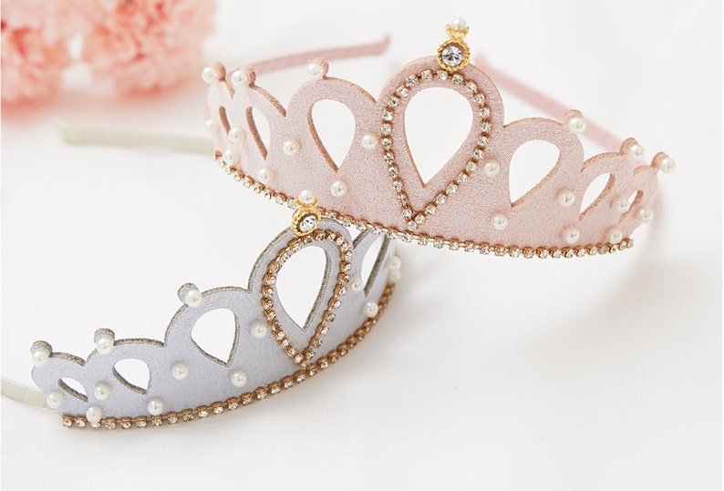 May include: Two princess crowns, one pink and one silver, with gold trim and pearl accents.
