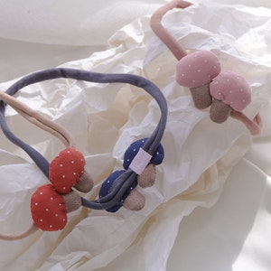 May include: Three fabric headbands with mushroom-shaped embellishments. The headbands are in pink, navy blue, and brown with white polka dots.