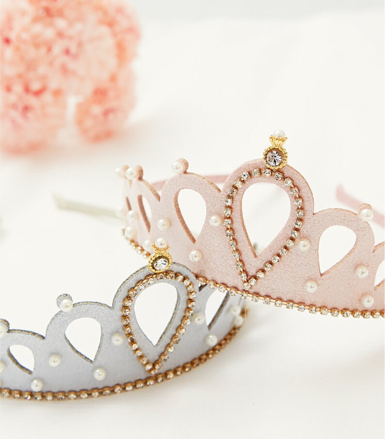 May include: Two princess crowns, one pink and one silver, with pearl and rhinestone accents. The crowns are made of felt and have a headband.