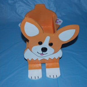 May include: A wooden orange and white dog-shaped planter with a white rim and black eyes. The planter has a small opening at the top for planting.