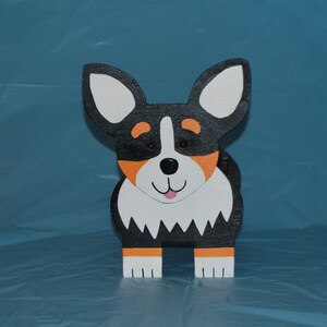 May include: A wooden figurine of a black and white dog with orange accents. The dog has a white face with black eyes and a pink tongue. The figurine is standing on a blue surface.