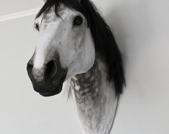 Puede incluir: Una escultura de cabeza de caballo montada en la pared con un pelaje gris moteado con manchas blancas y una crin oscura y fluida. El caballo tiene rasgos faciales realistas, incluyendo ojos oscuros, un hocico prominente y orejas erguidas.