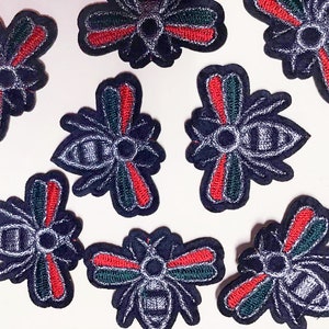 May include: A collection of nine embroidered iron-on patches featuring a bee design. The bees are black with silver accents and have red and green stripes on their wings.