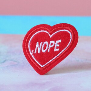 May include: Red felt heart-shaped patch with white embroidered text that says "NOPE".