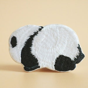 May include: Embroidered iron-on patch of a black and white panda bear lying down. The panda is facing to the right.