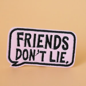 May include: Pink and black embroidered patch with the text "Friends Don't Lie."