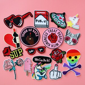 May include: A collection of colorful embroidered iron-on patches featuring various designs, including a skull with rainbow colors, a unicorn, a rose, a broken heart, a cat wearing sunglasses, a middle finger, and a cigarette pack with the text "FUK V".