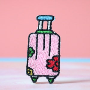 May include: Pink embroidered luggage patch with a green handle, green wheels, and a red flower design.