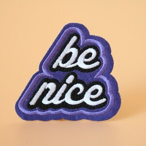 May include: Purple felt patch with the words "be nice" embroidered in white and black thread.
