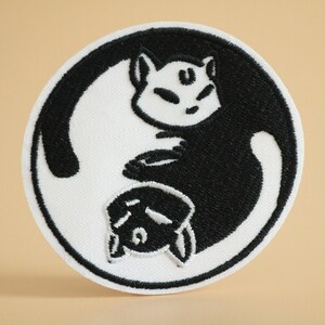 May include: Black and white embroidered patch featuring two cats in a yin yang design.