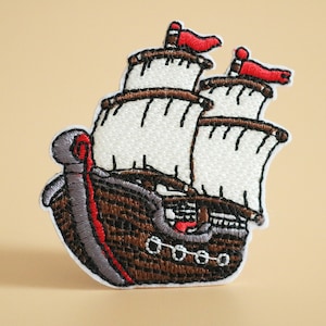 May include: Embroidered iron-on patch of a brown sailing ship with white sails and red flags.