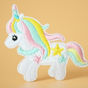 May include: White embroidered unicorn patch with a rainbow mane and tail. The unicorn has a yellow star on its side and a pink star on its leg.