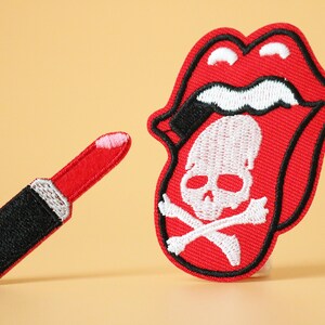 May include: Two embroidered iron-on patches. One is a red tongue with a white skull and crossbones. The other is a red lipstick.