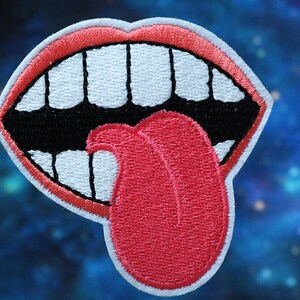 May include: Embroidered patch of a cartoon mouth with a red tongue sticking out. The mouth is open wide with white teeth and a black outline.