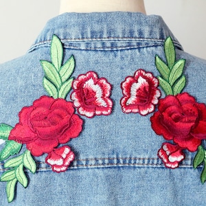 May include: A denim jacket with embroidered red roses and green leaves. The roses are in a cluster of three on each side of the jacket.