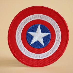 May include: A red, white and blue embroidered patch featuring a white star on a blue circle surrounded by a white circle and a red outer circle.