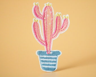 May include: A pink embroidered cactus with yellow accents in a blue and white striped pot.