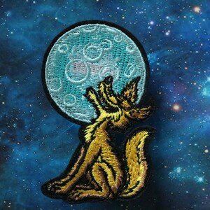May include: An embroidered patch of a yellow coyote howling at a blue moon with white craters. The moon is outlined in black.