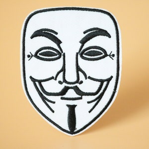 May include: White embroidered patch with a black outline of the Anonymous mask, featuring a stylised face with a wide smile and a goatee.