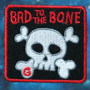 May include: Red and white embroidered patch with a skull and crossbones and the text "Bad to the Bone".