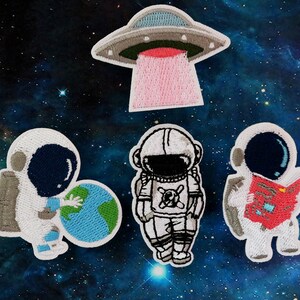 May include: Four embroidered iron-on patches featuring a UFO, a globe, and two astronauts. One astronaut is holding a globe, and the other is reading a book.