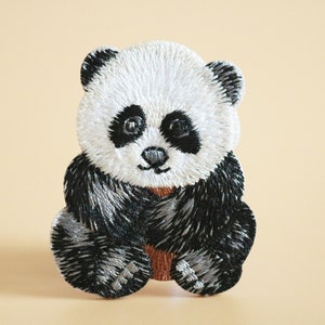May include: Embroidered panda bear patch with black and white fur. The panda is sitting with its paws in front of it.