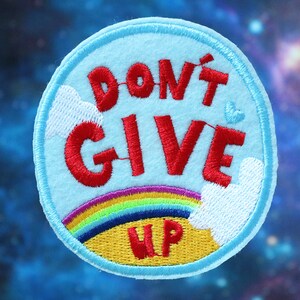 Könnte beinhalten: Ein gestickter Aufnäher in Blau und Gelb mit einem Regenbogen und Wolken. Der Text "DON'T GIVE UP" ist in Rot.
