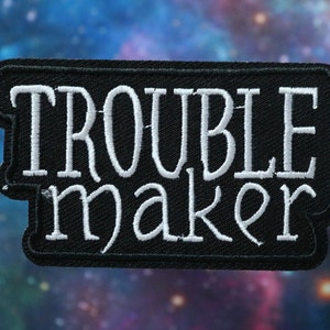 May include: Black embroidered patch with white stitching that reads "Trouble maker".