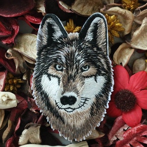 May include: Embroidered wolf head patch with brown, black, and white fur. The patch is surrounded by red and brown flower petals.