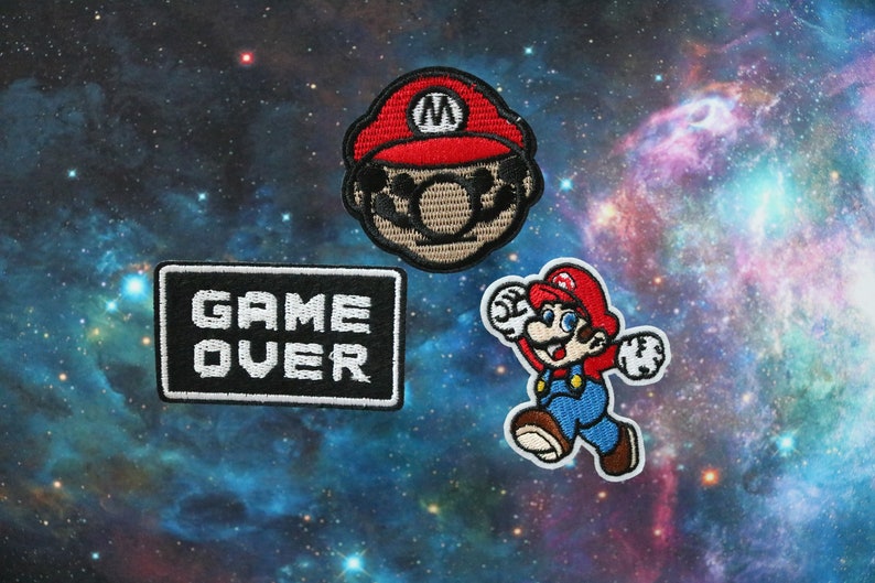 May include: Three embroidered iron-on patches featuring a red and black Mario character, a red and black Mario character running, and a black and white "GAME OVER" patch.