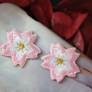 May include: Two pink and white embroidered cherry blossom flower patches with gold centers.