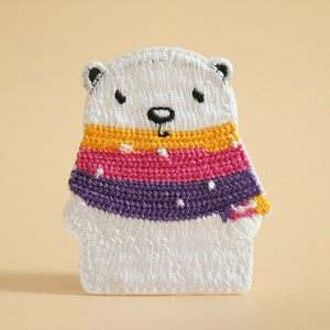 May include: White polar bear plush toy wearing a colorful striped scarf with yellow, pink, and purple stripes. The scarf has white polka dots.
