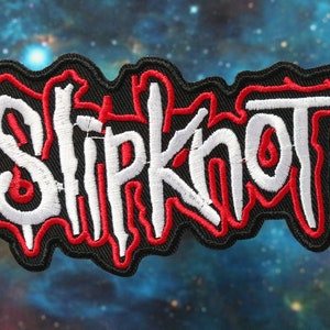 May include: A black embroidered patch with the word "Slipknot" in white and red lettering. The patch has a distressed, dripping look.